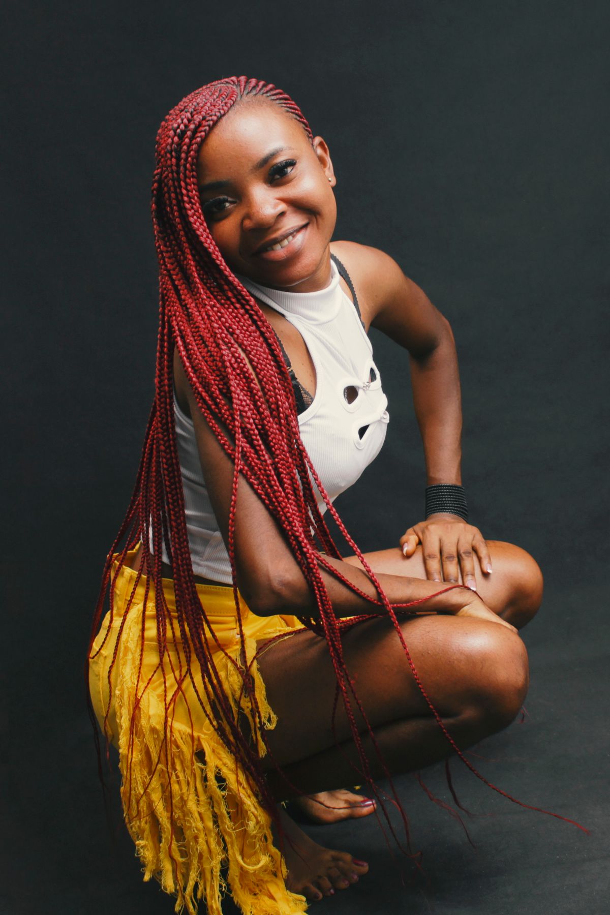 Portrait of a joyful woman with red braided hair posing in a colorful outfit in a studio setting.