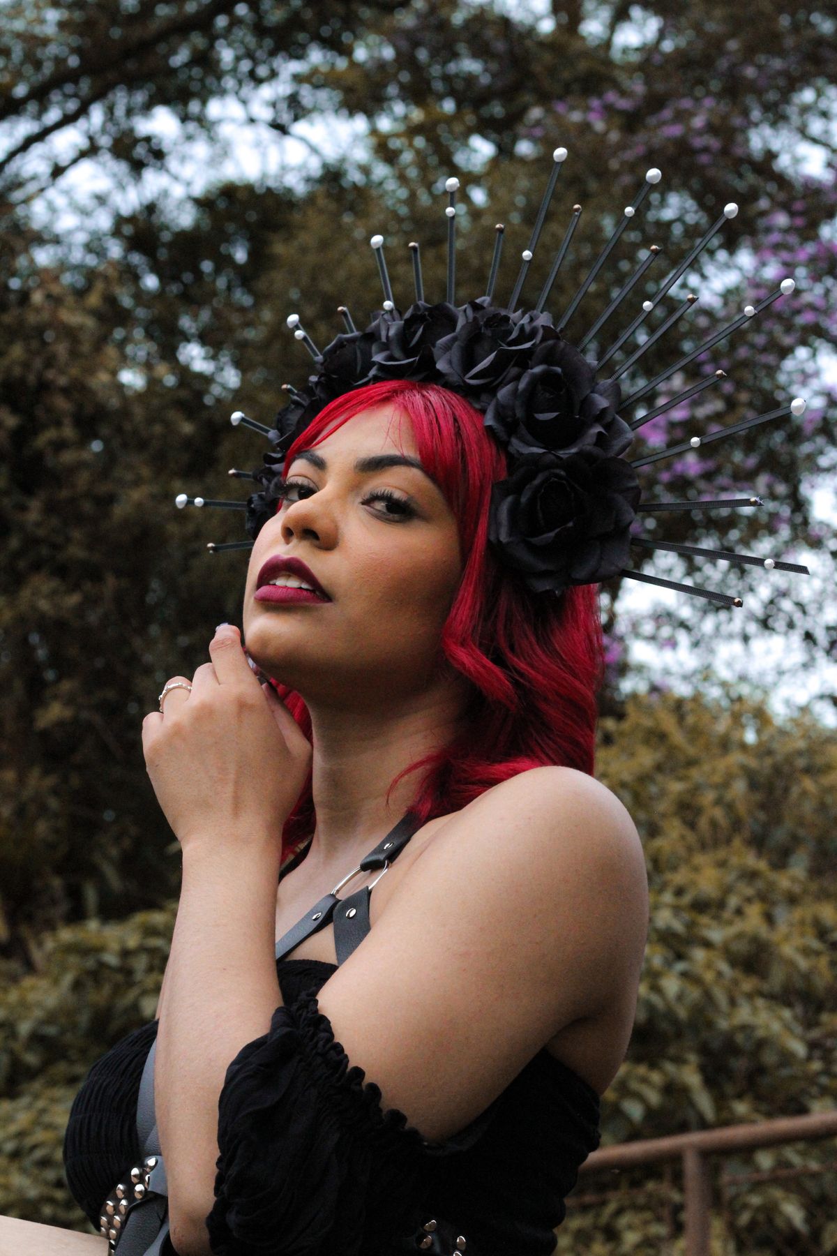 Fashion portrait of a woman with a striking black floral headdress and red hair posing outdoors.